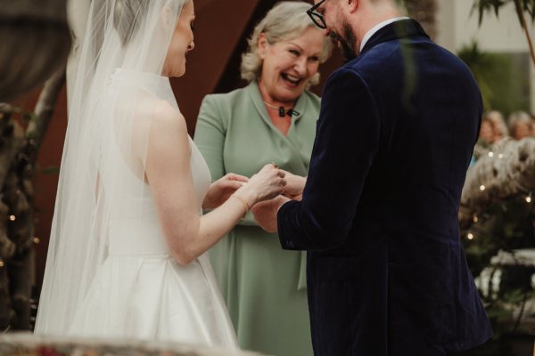 Officiant bride and groom smiling hand holding rings