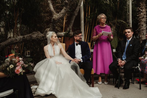 Officiant in pink speech during ceremony bride and groom