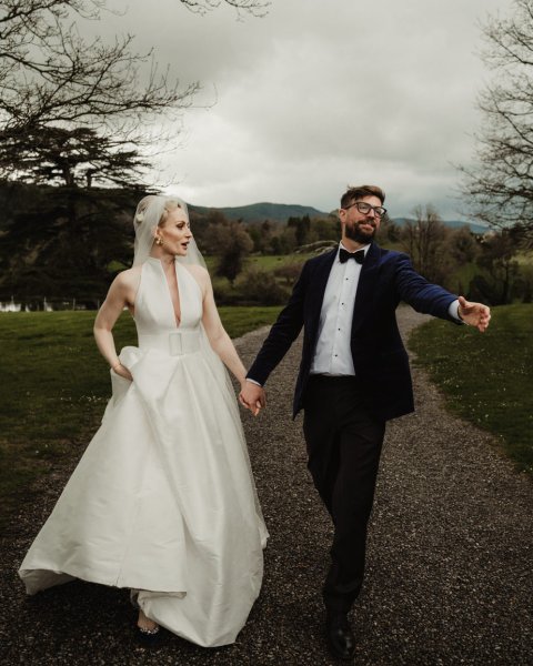 Bride and groom walking along pathway holding hands