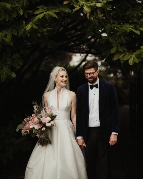 Bride and groom in park bouquet in hand