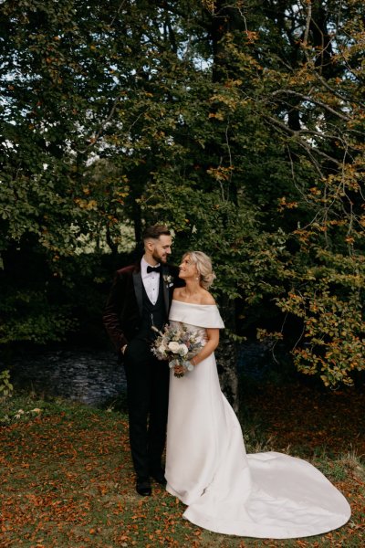 Bride and groom look at each other surrounded by trees in park