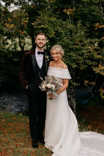 Bride and groom couple surrounded by trees in park smiling