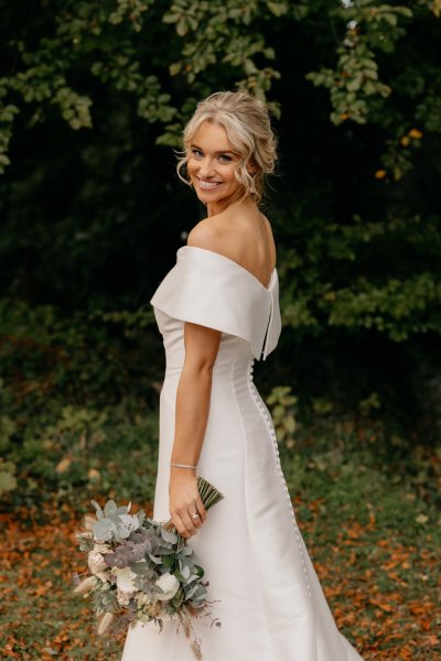 Bride surrounded by trees in park smiling holding bouquet