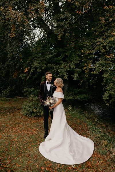 Bride and groom look at each other surrounded by trees in park