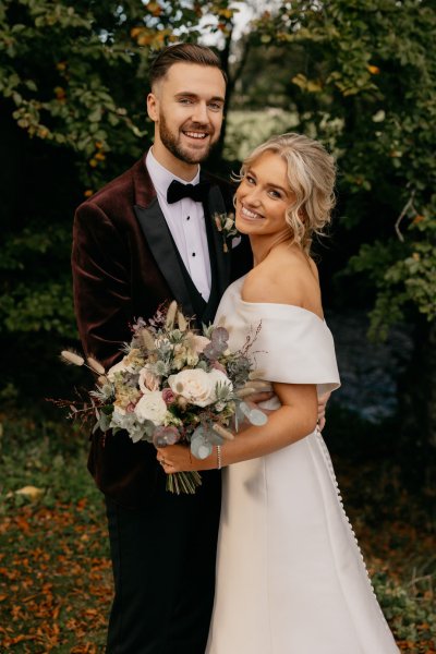 Bride and groom couple surrounded by trees in park smiling