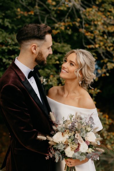 Bride and groom look at each other surrounded by trees in park