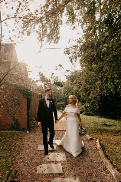 Bride and groom walk along pathway in forest/park holding hands sun is shining