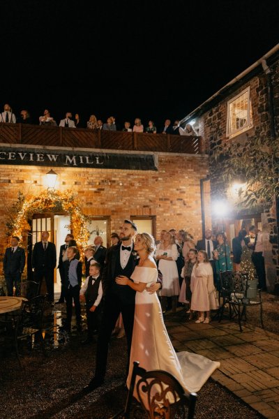 Couple bride groom and guests watch and look at firework display