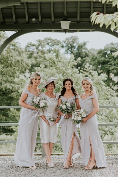 Bride and bridesmaids surrounded by trees in forest holding bouquet/flowers