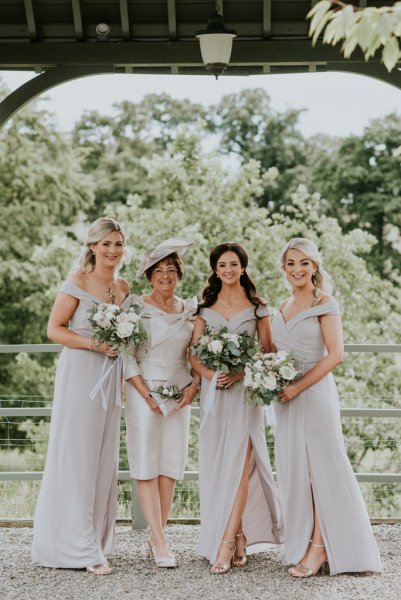 Bride and bridesmaids surrounded by trees in forest holding bouquet/flowers