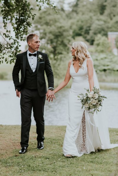 Lake in background bride and groom hold hands looking at each other