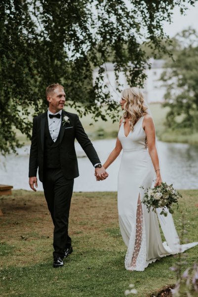 Lake in background bride and groom hold hands looking at each other