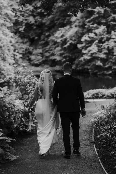 Black and white setting of bride and groom walking along forest pathway