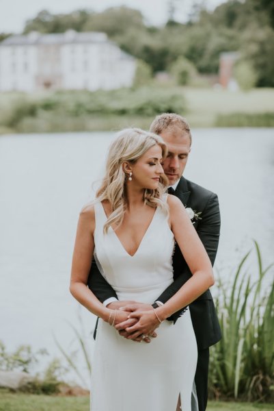 Grooms arms around bride lake in background