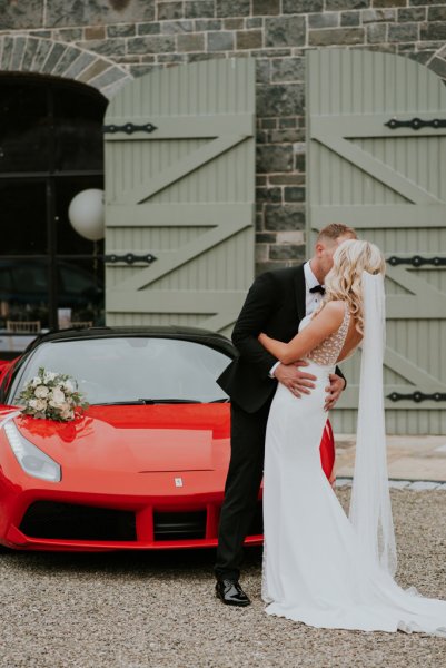 Bride and groom kiss in front of red sports car