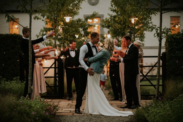 Mrs Summs denim jacket holding hands with groom kissing kiss in front of guests