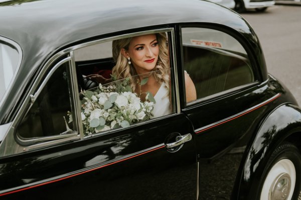 Bride sitting in black car smiling holding roses/flowers