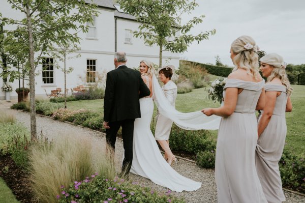 Bridesmaid holding veil walking with mother and father bride