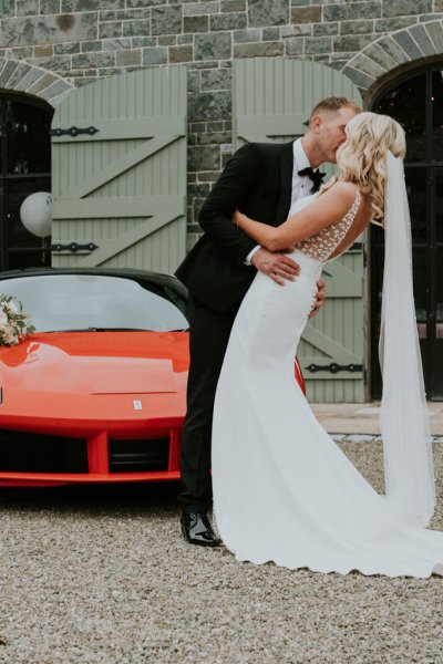 Bride and groom kiss in front of red sports car