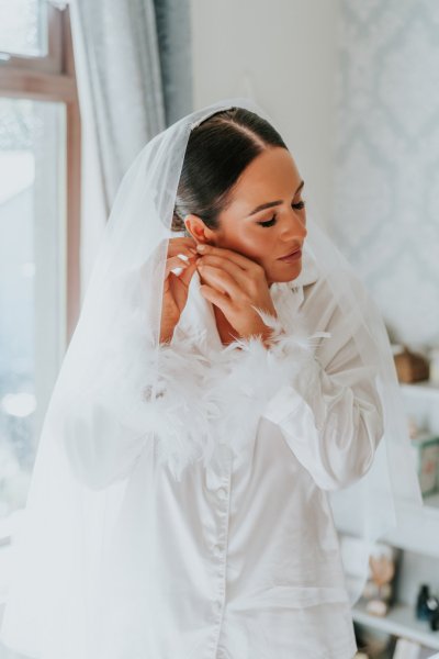 Bride putting on earrings feather bridalwear detail