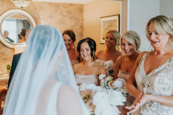 Bridesmaids holding flowers react to bride