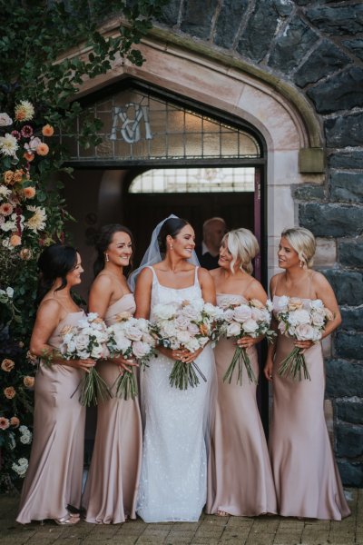 Bride and bridesmaids salmon coloured satin dresses roses bouquet flowers exterior church ceremony setting