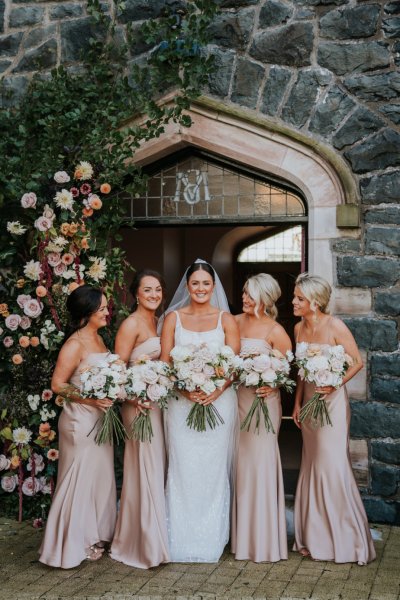 Bride and bridesmaids salmon coloured satin dresses roses bouquet flowers exterior church ceremony setting