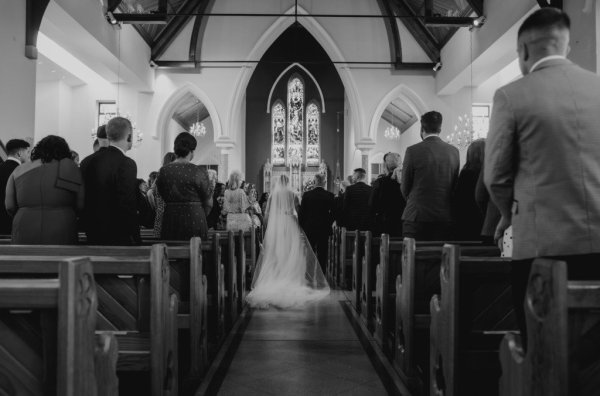 Black and white image of father of the bride walking up the aisle to groom