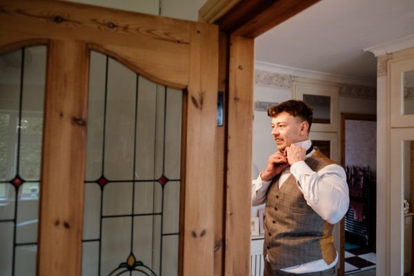 Groom in suit getting ready bow tie mirror