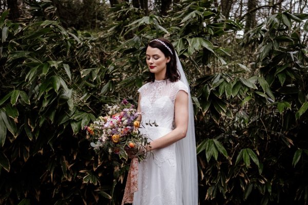 Bride in front of trees in forest park veil detail holding bouquet of flowers