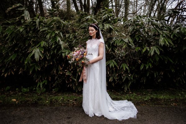 Bride in front of trees in forest park veil detail holding bouquet of flowers