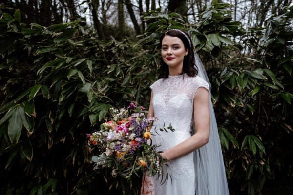 Bride in front of trees in forest park veil detail holding bouquet of flowers