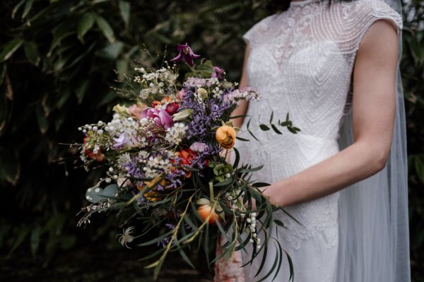 Bride in front of trees in forest park veil detail holding bouquet of flowers