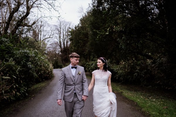 Bride and groom walk on the pathway in forest/park holding hands