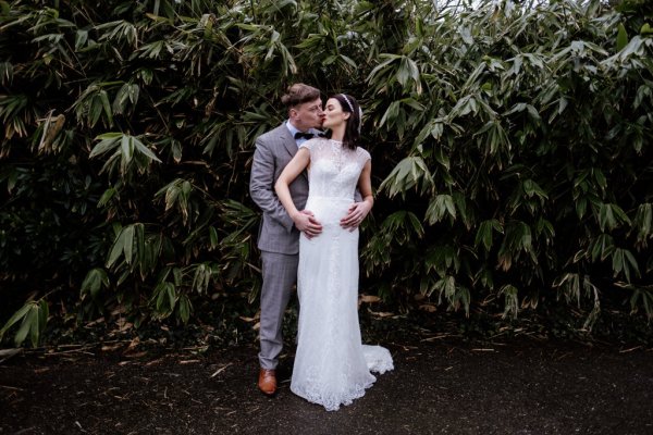 Groom has arms hands around brides waist in forest/park