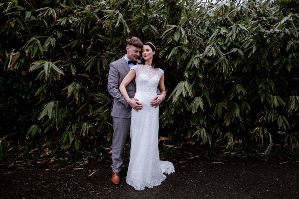 Groom has arms hands around brides waist in forest/park