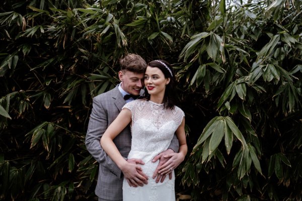 Groom has arms hands around brides waist in forest/park