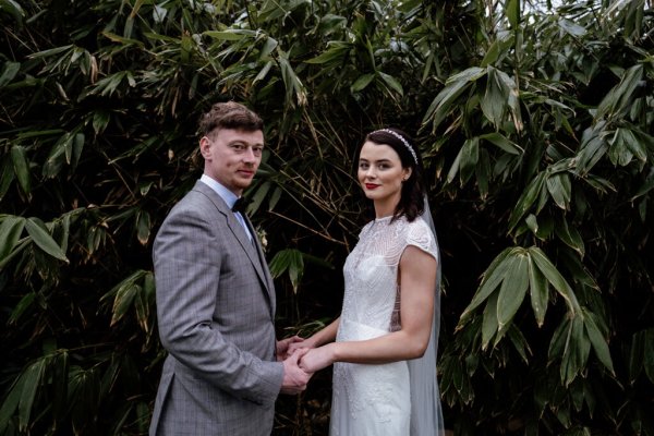 Bride and groom holding hands in front of tree in park/forest setting