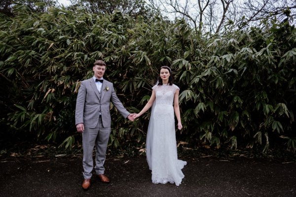 Bride and groom holding hands in front of tree in park/forest setting