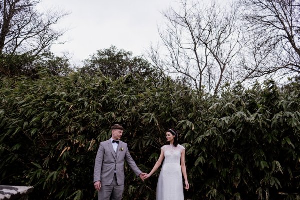 Bride and groom holding hands in front of tree in park/forest setting