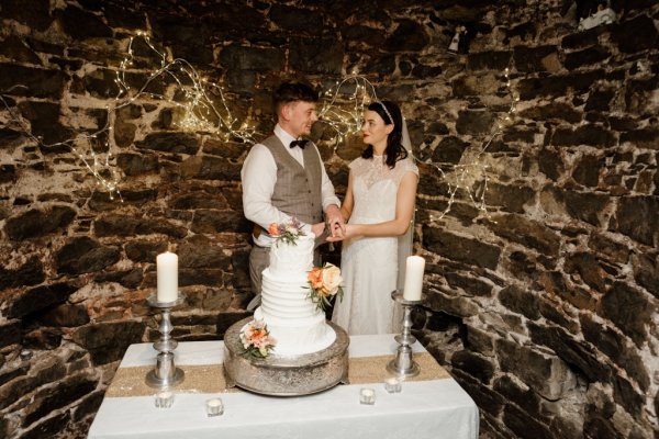 Bride and groom cut the white wedding cake with flowers on it