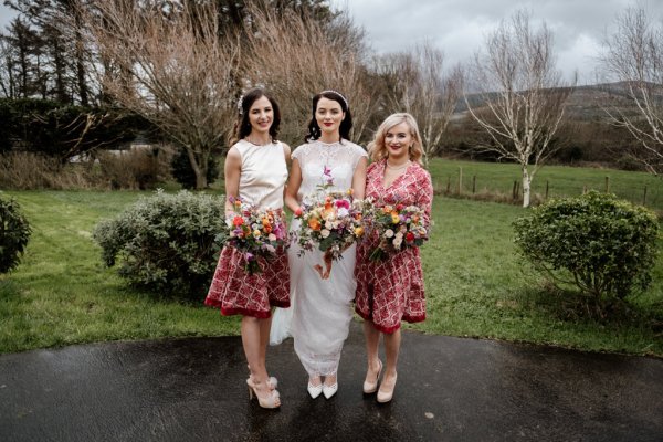 Bride and bridesmaids holding bouquet of flowers park grass setting trees