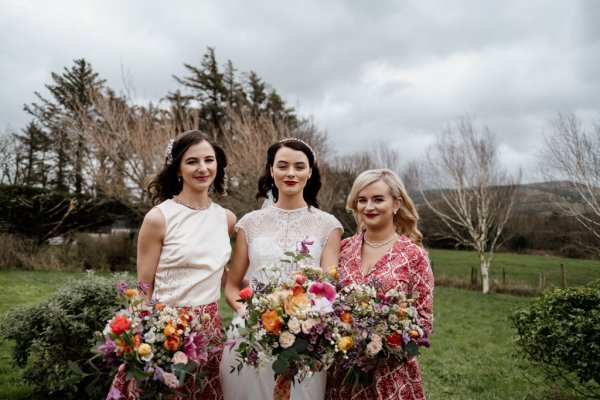 Bride and bridesmaids holding bouquet of flowers park grass setting trees