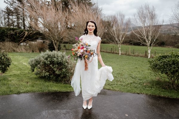 Bride standing grass holding flowers exterior shot park trees