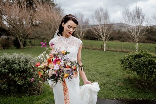 Bride standing grass holding flowers exterior shot park trees