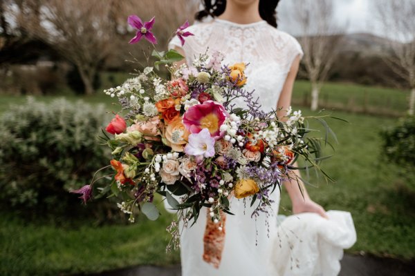 Bride standing grass holding flowers exterior shot park trees