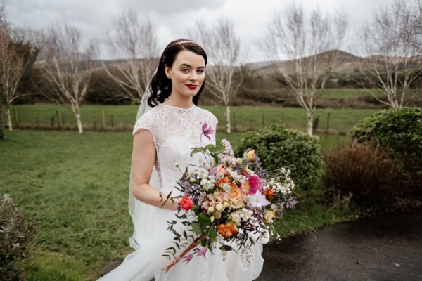 Bride standing grass holding flowers exterior shot park trees