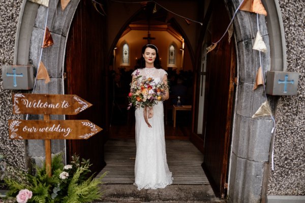 Bride standing at church exterior entrance holding flowers