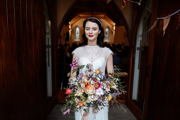 Bride standing at church exterior entrance holding flowers