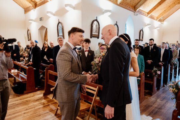 Father hands bride over to groom as they shake hands at alter